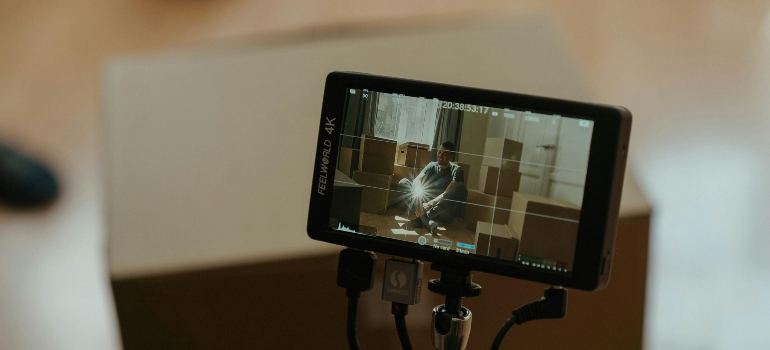 A camera screen showing a person among moving boxes, tied to Broker Can Help When Your Movers Cancel Last Minute.