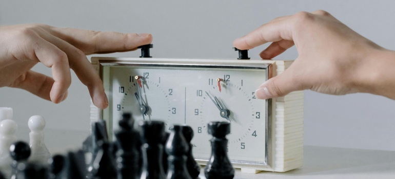 Close-up of two hands pressing a chess clock during a game, echoing Leaving Massachusetts for Florida decisions.