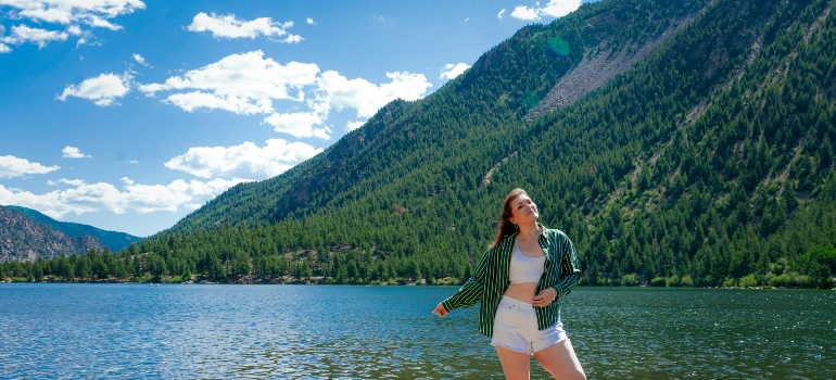 Fashionable woman enjoying summer by a mountain lake, reflecting lifestyle changes and what you need to know before moving to Colorado from New Jersey.
