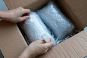 Woman packing fragile items wrapped in bubble wrap and shredded paper.