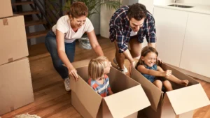 A man and a woman play with their kids as they pack moving boxes in their home.
