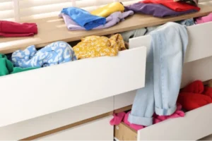A cluttered chest of drawers in need of organization overflowing with clothing items.